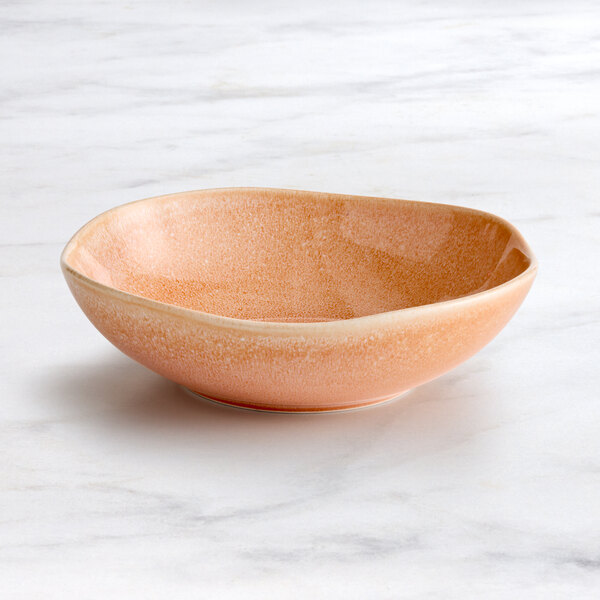 An Acopa Highlands primrose pink china bowl with an orange rim on a marble surface.