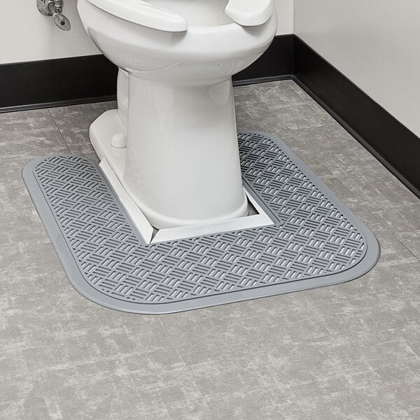 A toilet with a gray Lavex disposable floor mat in a bathroom.