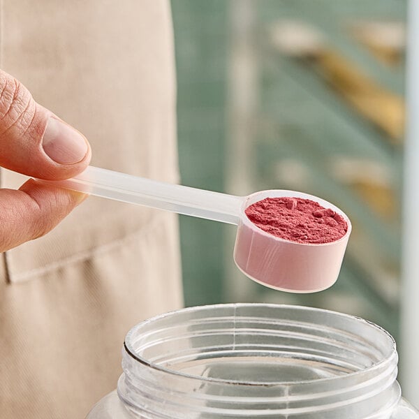 A person holding a long-handled polypropylene scoop full of pink powder.