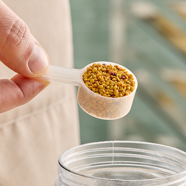 A person holding a 14.8 cc polypropylene scoop filled with seeds.