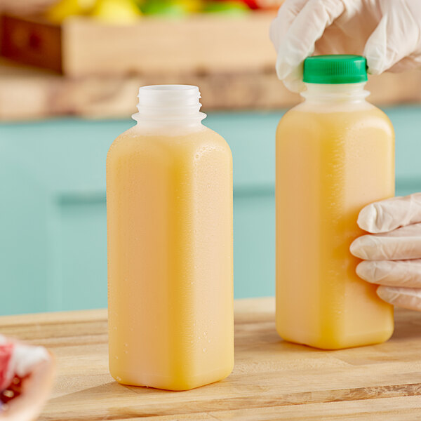 A pair of gloved hands holding translucent HDPE square bottles of yellow liquid.