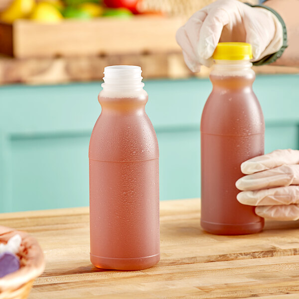A gloved hand holds a translucent plastic bottle of liquid on a table.