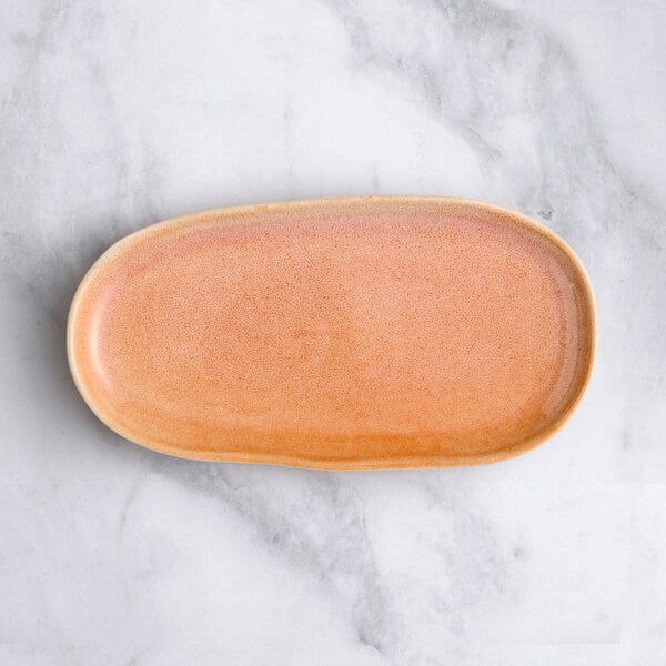 An Acopa Primrose peach coupe tray with an oval shape and pink rim.