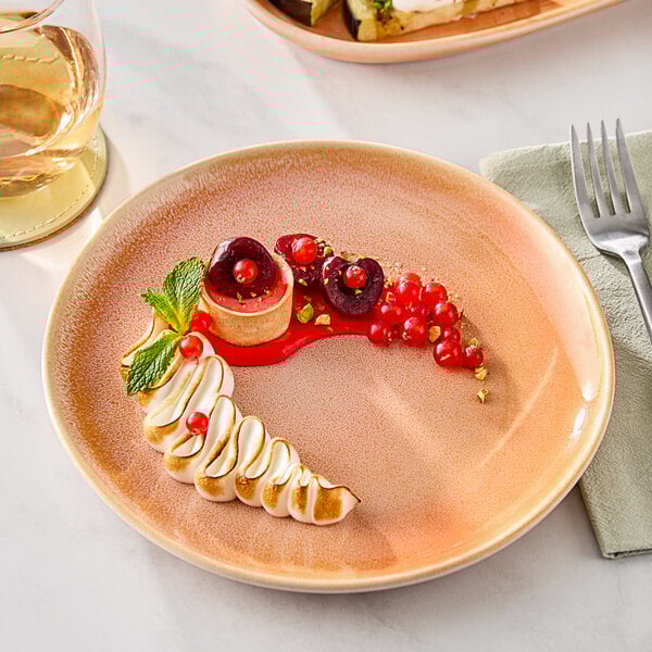 A Acopa Highlands Primrose Peach coupe plate with dessert on it next to a glass of wine.