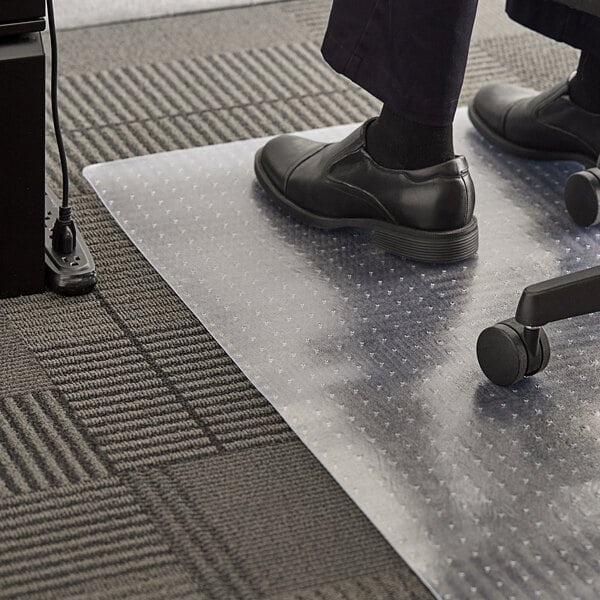 A person standing on a 360 Office Furniture clear plastic mat with black shoes on.