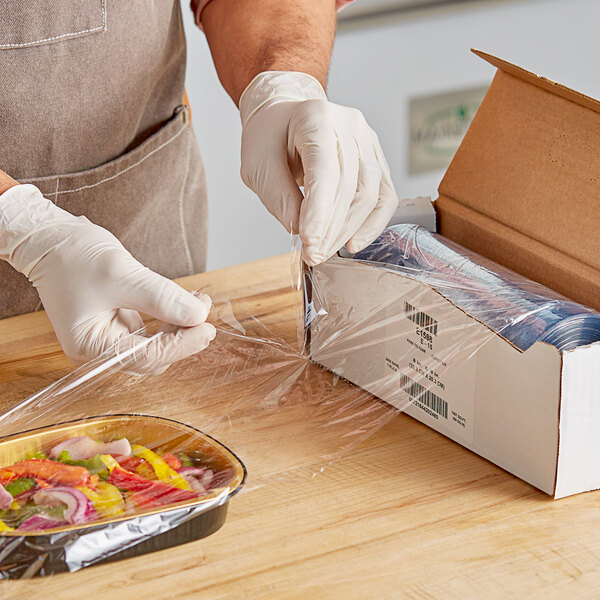 A hand in a glove using Anchor Packaging perforated plastic wrap to cover a box of food.