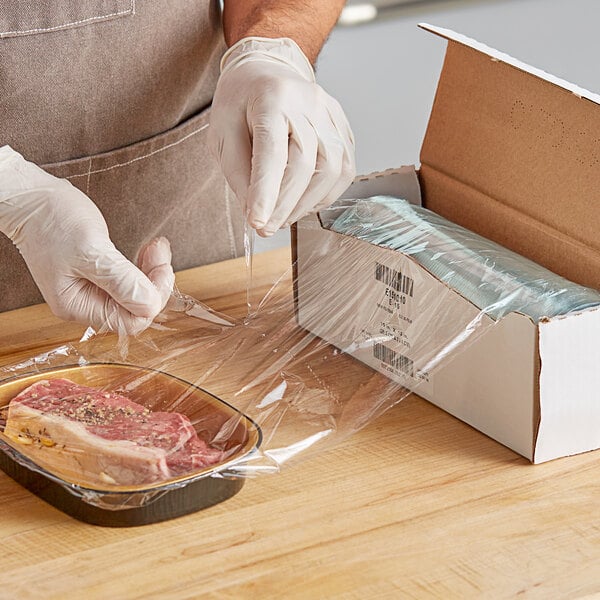 A person wearing gloves wrapping a piece of meat in Anchor Packaging perforated plastic wrap.