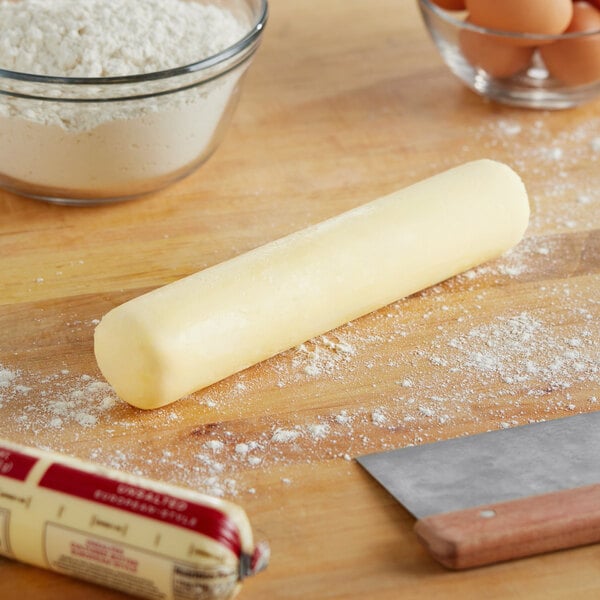 A rolled up dough on a table with a knife and a bowl of flour.