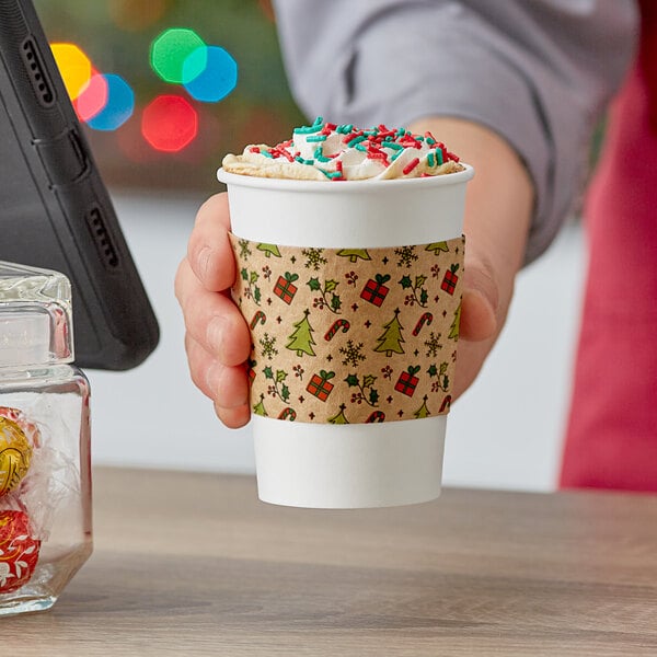 A person holding a holiday printed Choice coffee cup with a sleeve on it.