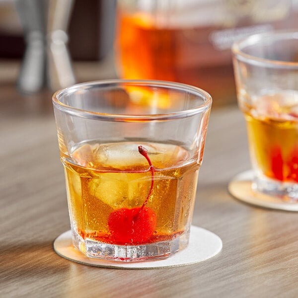 Two Acopa Memphis rocks glasses with whiskey and cherries on a table.