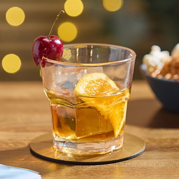 An Acopa Memphis old fashioned glass of whiskey with a cherry and a slice of orange on a table.