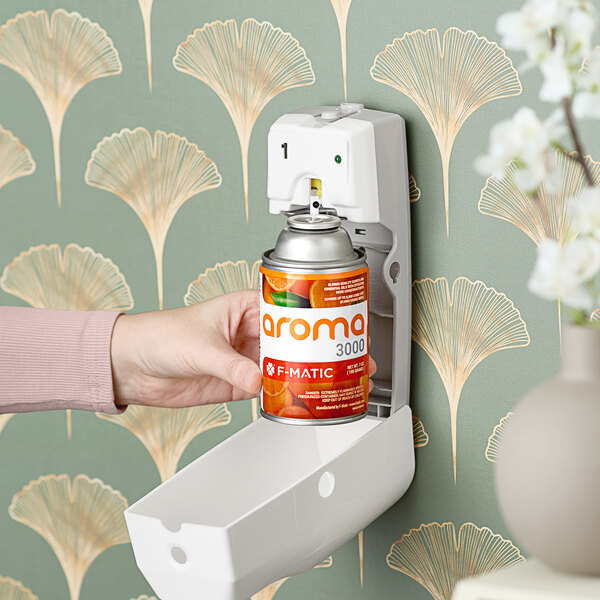 A person putting a F-Matic Citrus Sunburst air freshener refill into a wall-mounted air freshener.