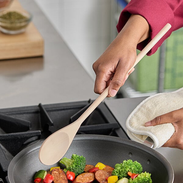A person cooking food in a pan with a Choice 16" wooden spoon.