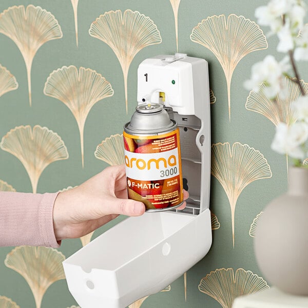 A person putting a can of F-Matic Ripe Mango air freshener into a wall-mounted dispenser.