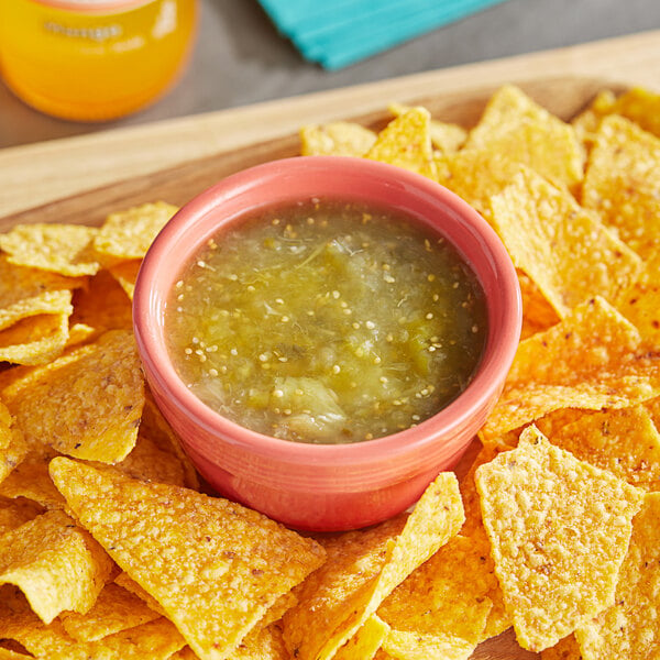 A bowl of green sauce with chips on a table.