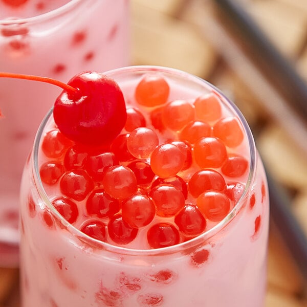 A glass of pink liquid with Bossen Sour Cherry Bursting Boba and a cherry on top.