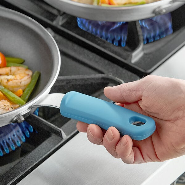 A hand using a blue Vigor pan handle sleeve to hold a pan of food.