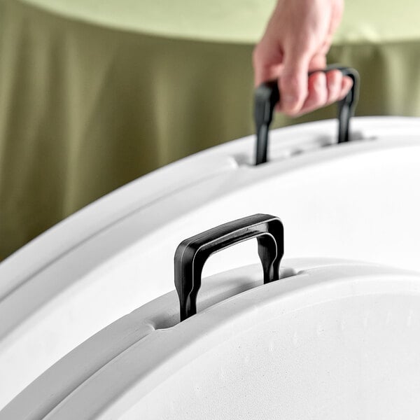 A hand holding a white plastic Lancaster Table & Seating tray with handles.
