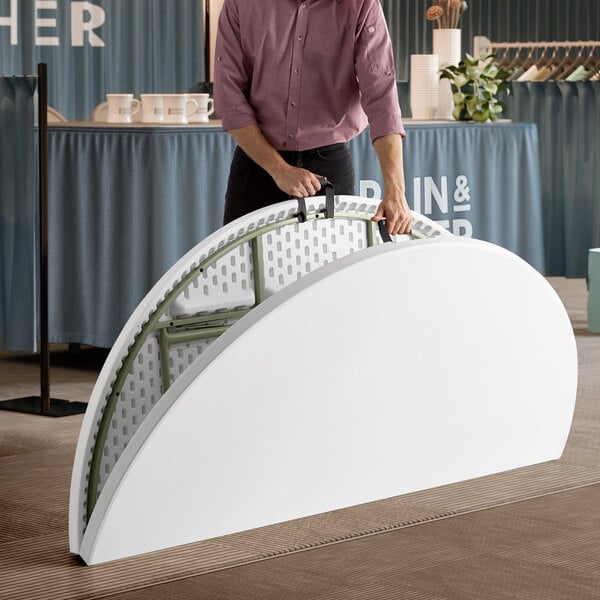 A man holding a Lancaster Table & Seating white plastic bi-folding table.