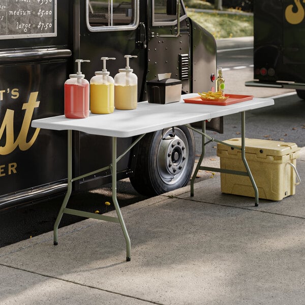 A Lancaster Table & Seating granite white plastic folding table set up with food containers and bottles of liquid.