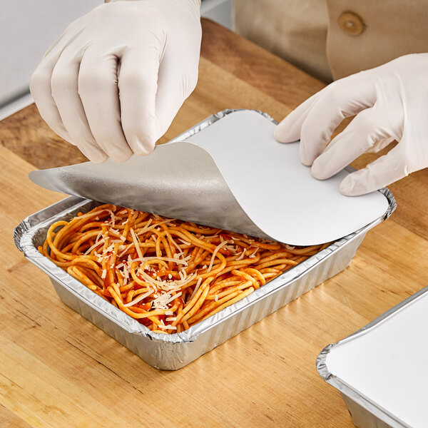 A person in white gloves putting food in a Western Plastics foil container.