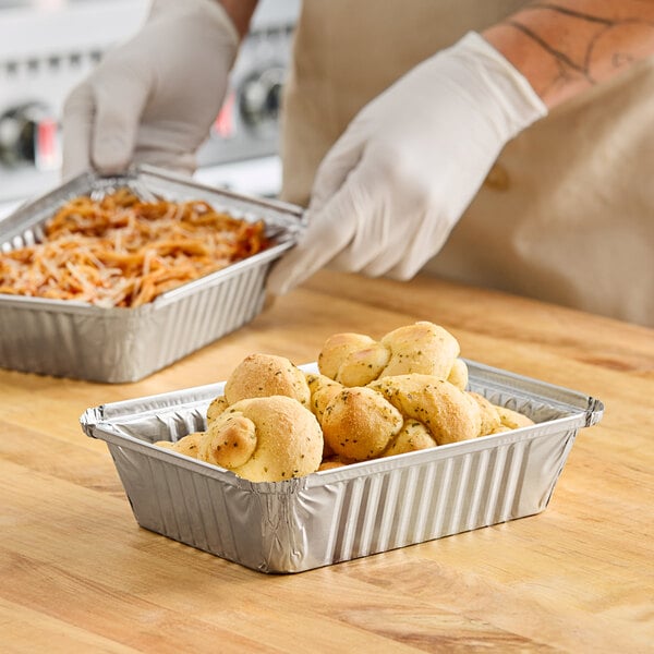 A gloved hand preparing food in a Western Plastics oblong foil take-out container.