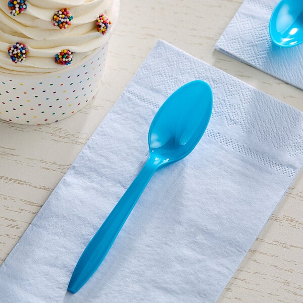 A blue plastic teaspoon on a white napkin next to a cupcake.