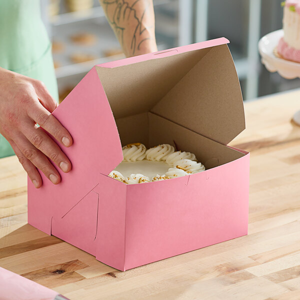 A person opening a Southern Champion pink bakery box to reveal a cake inside.
