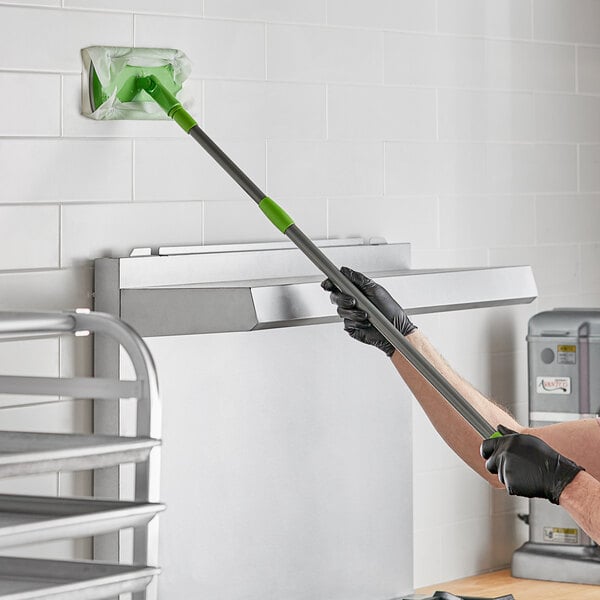 A person using a Sani Professional extendable wand to clean a wall in a professional kitchen.