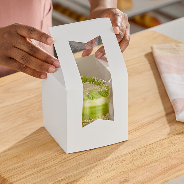 A person holding a white Southern Champion cake box with a piece of cake inside.
