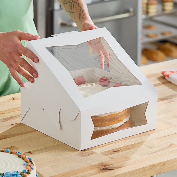 A person holding a Southern Champion cake in a white box with a window.