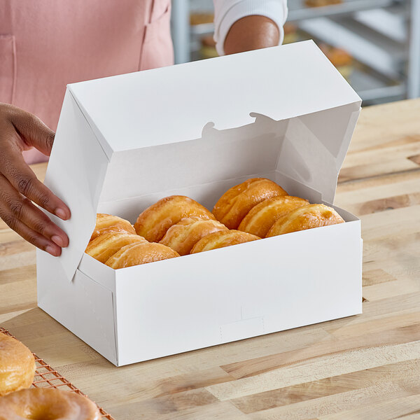 A woman's hand holding a white Southern Champion donut box on a table.