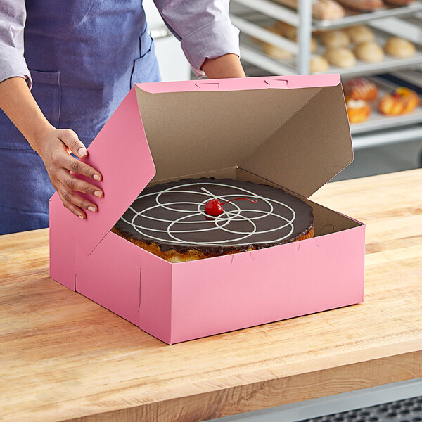 A woman holding a Southern Champion pink cake box with a cake inside.