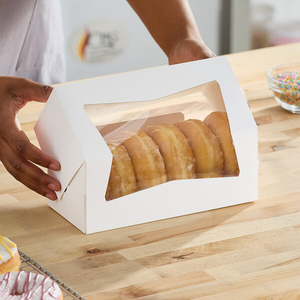 A person holding a Southern Champion white donut box on a table.