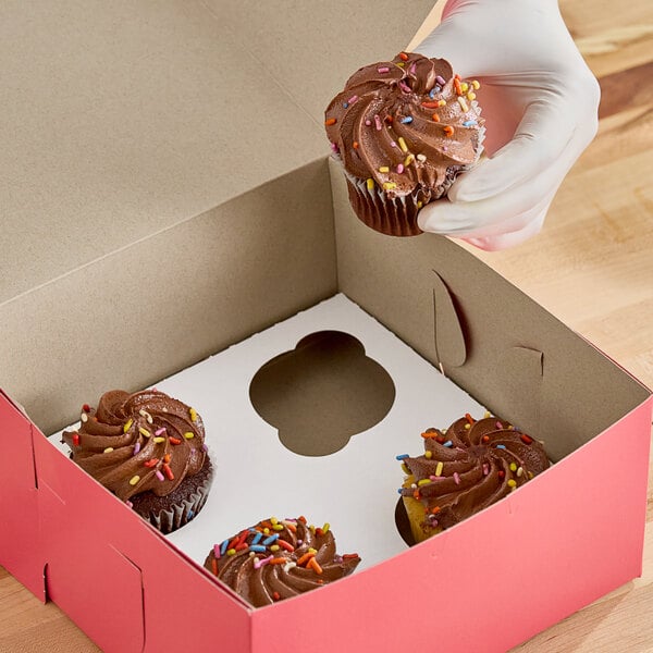 A hand placing a chocolate cupcake with sprinkles into a Southern Champion cupcake box.