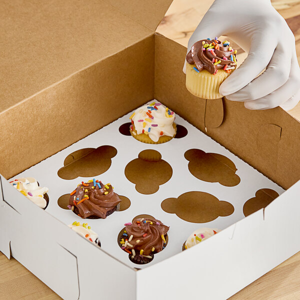 A hand putting a chocolate frosted cupcake with sprinkles in a Southern Champion cupcake box.