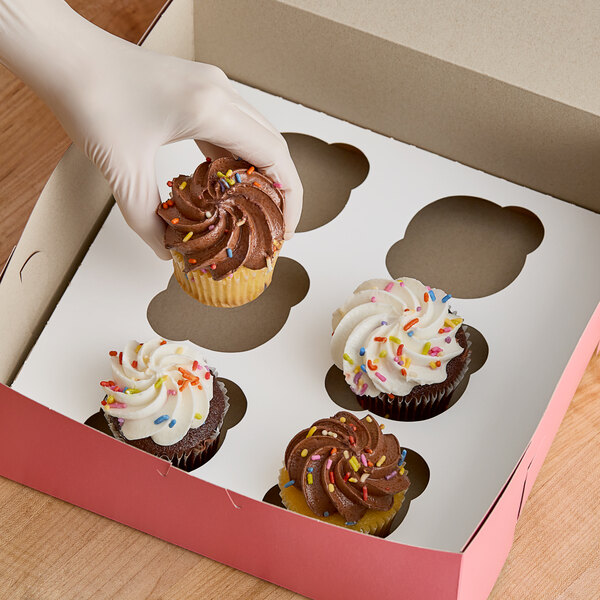 A hand places a cupcake with white frosting and sprinkles into a bakery box with a Southern Champion cupcake insert.
