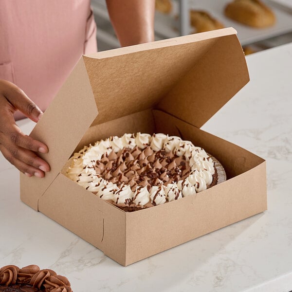 A person holding a Southern Champion Kraft bakery box filled with chocolate cake with white frosting.