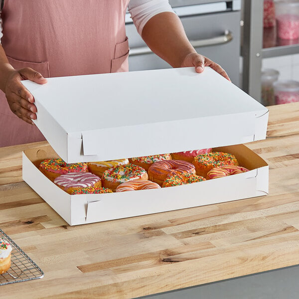 A woman holding a white Southern Champion Bakery Box filled with donuts.