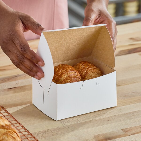 A person opening a Southern Champion white bakery box of croissants on a counter.