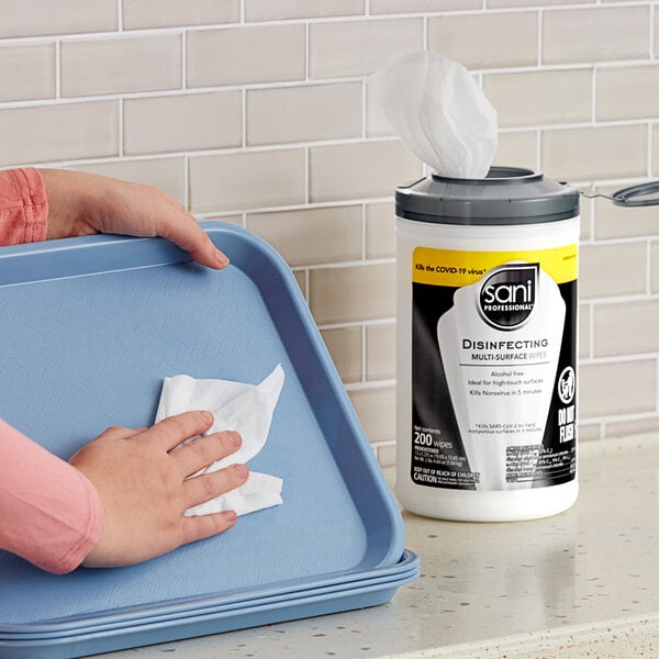 A person using a Sani Professional disinfecting wipe to clean a table tray.
