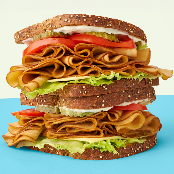 A large sandwich with Tofurky Next-Gen Vegan Roasted Turk'y Deli Slices and vegetables.