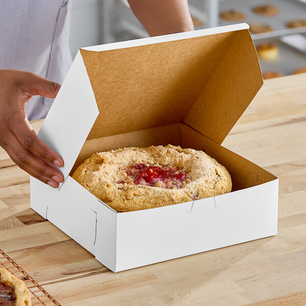 A person's hand putting a pastry in a Southern Champion white pie box.