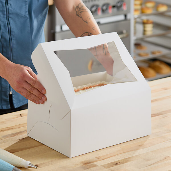 A person putting a doughnut into a Southern Champion bakery box with a plastic window.