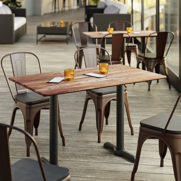 A Lancaster Table & Seating Excalibur table with a textured Yukon oak finish on a patio with chairs.