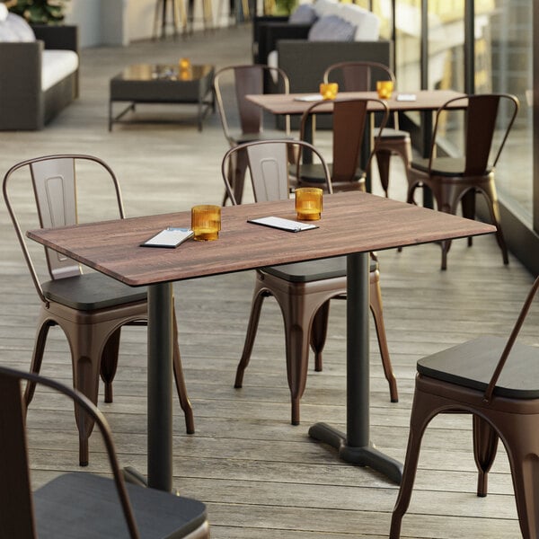 A Lancaster Table & Seating rectangular table with a textured walnut finish on a patio with chairs.