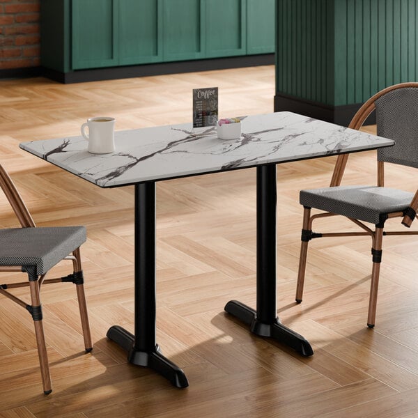 A rectangular table with a white marble-like top featuring dark veining, supported by two black pedestal legs, with two chairs placed on either side.