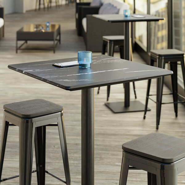 A Lancaster Table & Seating square table top with a black smooth finish on a table with stools.
