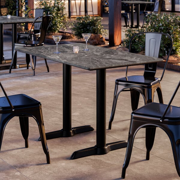 A rectangular outdoor table with a dark, marble-like surface and black metal legs, surrounded by black metal chairs, set on a patio.