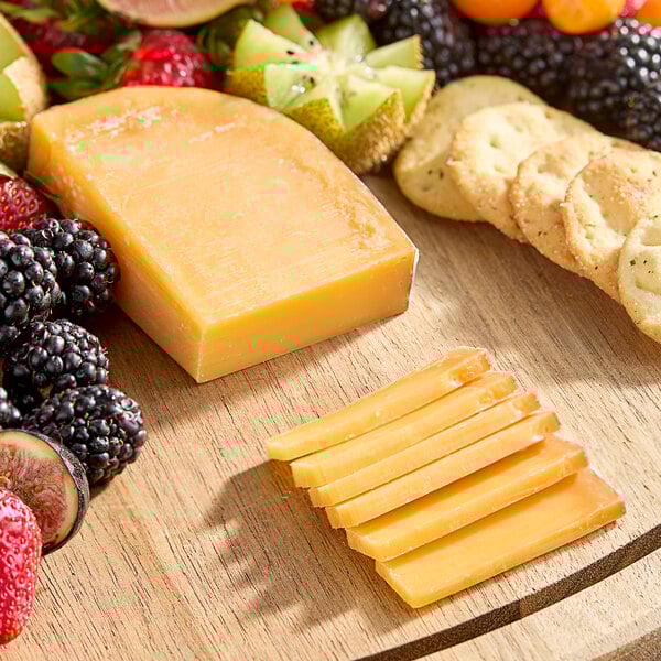 A wooden board with a block of Beemster Classic 18 Month Aged Gouda cheese next to fruit.